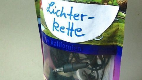 Eine wiederverwendbare Tüte mit Faltboden hält eine Lichterkette, beschriftet mit „Lichterkette“, in einem modernen Raum.
