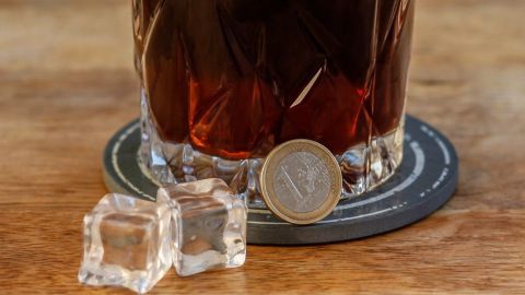 Ein stilvoller Tiki-Wumm-Drink steht auf einem Untersetzer, umgeben von Eiswürfeln und einer Münze auf einem Holztisch.