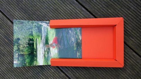 Ein papierner Bilderrahmen zeigt ein Foto mit einer Landschaft, während er auf einer Holzoberfläche liegt.