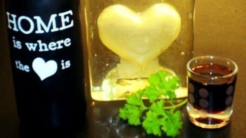 Eine Flasche Petersilienwein steht neben einem gefrorenen Herz und einem kleinen Glas, umgeben von frischer Petersilie.
