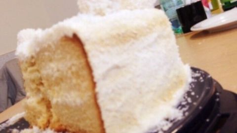 Ein schneeweißer Raffaello Kuchen steht auf einem Tisch, umgeben von Getränken und Geschirr, mit einer portionierten Seite.
