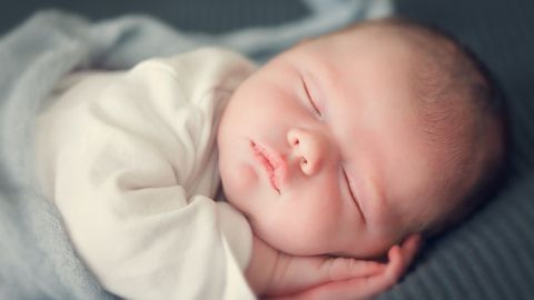 Ein schlafendes Baby liegt auf einer weichen Decke, das Gesicht friedlich und entspannt, umgeben von sanften Farben.