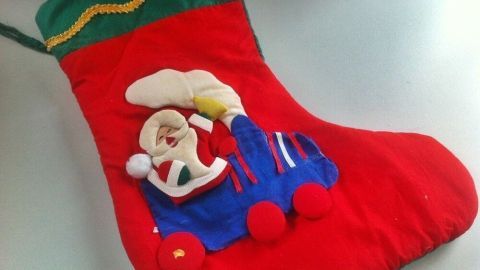 Ein roter Adventskalender-Strumpf mit einem fröhlichen Weihnachtsmann im blauen Auto und einer großen Süßigkeit.