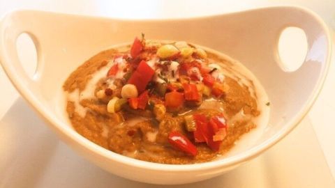 Eine cremige Linsensuppe mit Kokosmilch, garniert mit frischen Tomaten und Nüssen, in einer weißen Schüssel serviert.