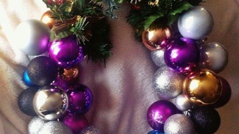 Ein bunter Türkranz aus Christbaumkugeln hängt an einem Drahtkleiderbügel, umgeben von einem weichen, hellen Stoff.