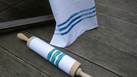 Ein Nudelholz liegt auf einem Holzboden, während eine gestreifte Stoffserviette darüber hängt.