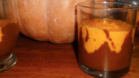 Kürbispudding in Gläsern zeigt strahlende Schichten aus Schokolade und Orange, mit einem Kürbis im Hintergrund.