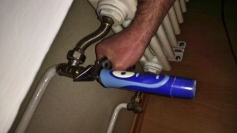 Ein Handwerker hält mit einer Zange ein Thermostatventil an einem Heizkörper, um es zu prüfen oder zu reparieren.