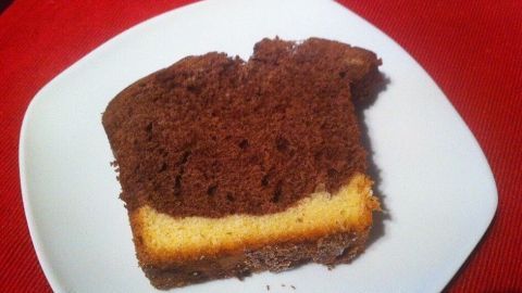 Ein Stück Nutella-Kokos-Marmorkuchen liegt auf einem weißen Teller, auf rotem Untergrund, mit einer nahtlosen Schicht aus Schokolade und Vanille.