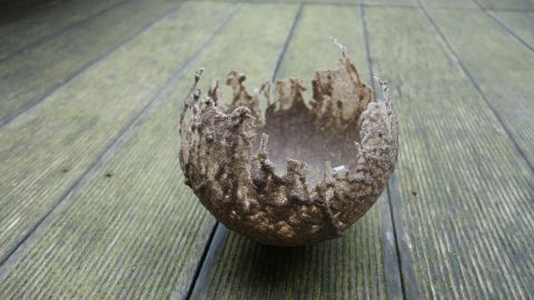 Eine zerbrochene Sandschale steht auf einem Holzfußboden, umgeben von natürlichem Licht und vermittelt handwerkliche Kreativität.
