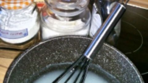 Ein Kochtopf mit einer cremigen Mischung, während Zutaten für ein WC-Gel wie Mondamin und ätherische Öle vorbereitet werden.