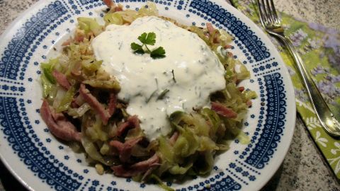 Ein frischer Spitzkohl-Salat mit Schinkenstreifen und einer cremigen Sauce, angerichtet auf einem gemusterten Teller.