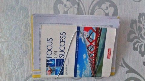 Ein Drahtkleiderbügel hält ein aufgeschlagenes Buch mit dem Titel "FOCUS ON SUCCESS" an einer Wand mit Muster.