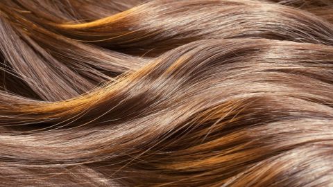Gesundes und glänzendes Haar strahlt in sanften Wellen und zeigt eine lebendige, warme Farbnuance im Detail.