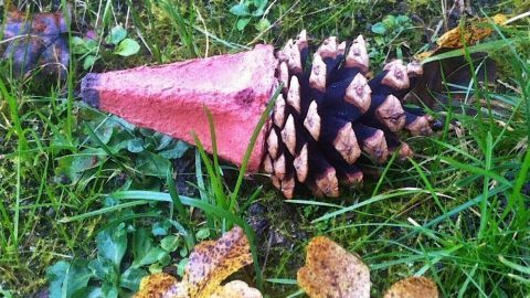 Ein Igel aus einem Zapfen und einem Eierkarton liegt auf grünem Gras, umgeben von bunten Herbstblättern.