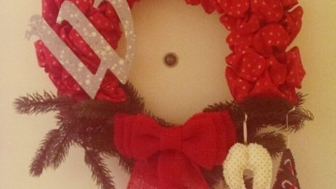 Ein rot gefärbter Türkranz mit Schleifen und Dekorationen hängt an einer Wand, um festliche Stimmung zu verbreiten.