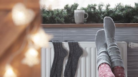 Socken liegen neben den Füßen auf einem warmen Heizkörper, während eine Tasse auf der Fensterbank steht und eine gemütliche Atmosphäre schafft.
