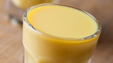 Ein transparenter Schnaps mit einer leuchtend gelben Eierlikör-Konsistenz steht auf einem Holzuntergrund.