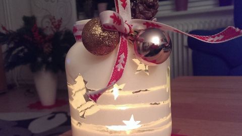 Ein dekoratives Windlicht leuchtet sanft, umgeben von festlichen Sternen und einer roten Unterlage, ideal für die Adventszeit.