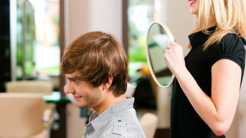 Ein Friseur zeigt einem Kunden mit einem Spiegel die frisierten Haare, während der Salon einladend wirkt.