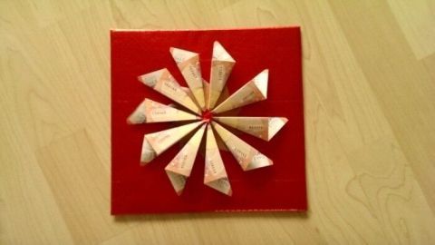 Ein Weihnachtsstern aus Geldscheinen ist auf rotem Untergrund kreativ angeordnet, um festliche Dekoration zu bieten.