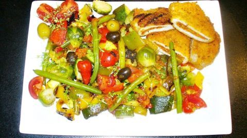 Pesto-Putenschnitzel liegt neben buntem, knackigem Ofengemüse auf einem weißen Teller, umgeben von einem dunklen Hintergrund.