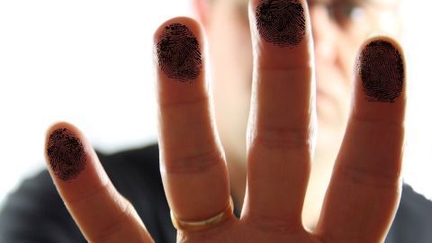 Fingers mit Druckertinte sind sichtbar, während eine Person frustriert im Hintergrund steht, was die Reinigung schwieriger macht.