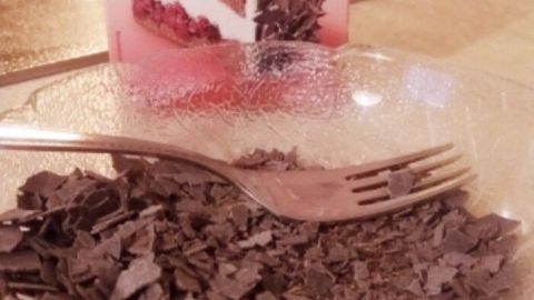 Raspelschokolade liegt in einer Schüssel, während eine Gabel daneben auf der Theke steht. Im Hintergrund ist die Verpackung sichtbar.
