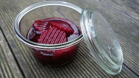 Ein Glas mit eingelegter Rote Bete steht auf einem Holzuntergrund, während der Deckel leicht geöffnet ist.