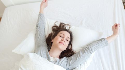 Eine Person liegt entspannt im Bett, streckt sich nach dem Aufwachen und fühlt sich ausgeruht, um luzides Träumen zu erleben.