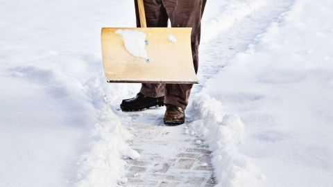 Eine Person mit einer Schneeschaufel räumt verschneiten Gehweg in einer schneebedeckten Umgebung während des Winterdienstes.