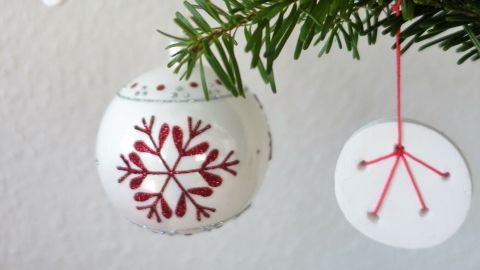 Schöne Christbaumkugeln aus Modelliermasse hängen an einem Weihnachtsbaum, umgeben von grünen Tannenzweigen.