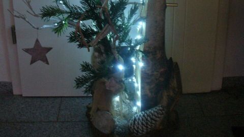 Eine kreative Außendekoration aus Holz mit Lichtern und Zweigen, die festlich am Hauseingang leuchtet.