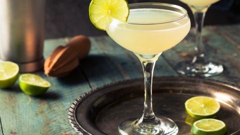 Ein eleganter Sommercocktail mit Lillet steht in einem Glas auf einem silbernen Tablett, umgeben von frischen Limettenscheiben.
