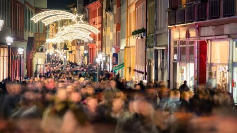 Eine belebte Straße wird von festlicher Beleuchtung erhellt, während Menschenmengen Geschenke suchen.