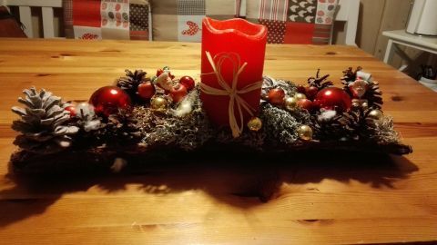 Ein roter Weihnachtskerzenhalter mit Tannenzapfen und glänzenden Kugeln schmückt einen Holztisch im (Schwarz)wald-Stil.