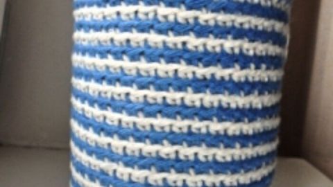 Ein blau-gestreifter Topflappen-Stulpen umhüllt ein Schraubglas und steht auf einer weißen Oberfläche.