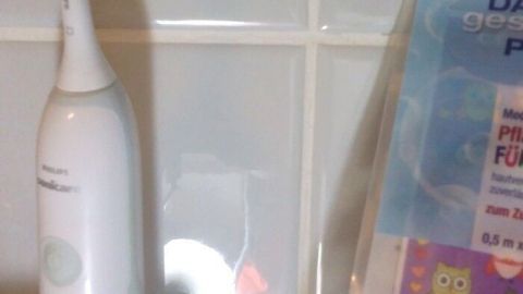 Eine Philips Sonicare Schallzahnbürste steht auf einem Badewannenregal, bereit zum Zähneputzen. Daneben ist ein hygienisch verpacktes Zahnpflegeprodukt zu sehen.