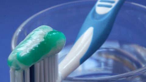 Eine Zahnbürste mit grüner Zahnpasta steht in einem Glas, bereit zur Anwendung gegen Aphten in einem neutralen Umfeld.