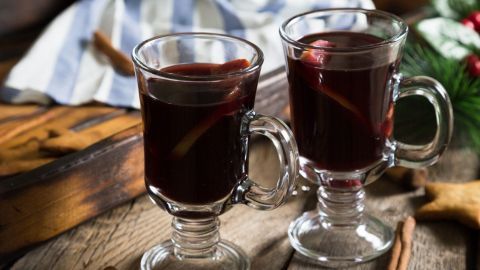 Zwei Gläser mit heißem Glühwein stehen auf einem rustikalen Holztisch, umgeben von Zimtstangen und Weihnachtsdekoration.