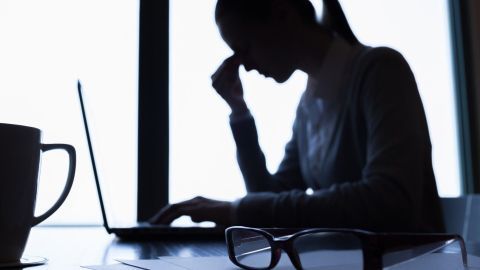 Eine person sitzt frustriert am Laptop, umgeben von einer Tasse Kaffee und einer Brille im Sonnenlicht.