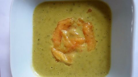 Eine grüne Erbsen-Estragon-Suppe mit Mangodip befindet sich in einer weißen Schüssel, umgeben von einem neutralen Hintergrund.