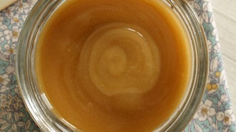 In einem Glasbehälter liegt glänzender Manuka Honig, der auf einem blumigen Tuch platziert ist, bereit zur Verwendung bei Nasennebenhöhlenentzündung.