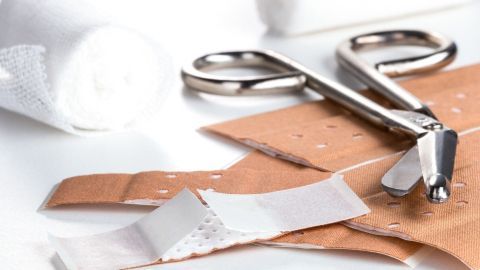 Verbandmaterialien und Scheren liegen auf einer weißen Oberfläche, bereit zum Anlegen von Pflastern bei einer Wunde.