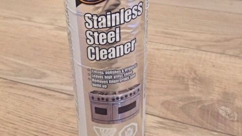 Ein Spray für die Reinigung von Edelstahl steht auf einem klaren, holzähnlichen Fußboden. Es zielt darauf ab, Klebereste zu entfernen.