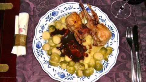 Auf einem Teller liegen gebratene Wachteln mit Portweinsauce, umgeben von Salzkartoffeln und Rosenkohl, angerichtet auf einem eleganten Tisch.