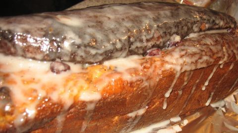 Eine Cranberry-Stolle liegt auf glänzendem Papier, überzogen mit einer süßen Glasur, die vom oberen Rand tropft.