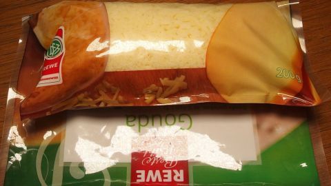 Eine Verpackung mit geriebenem Käse liegt auf einem Tisch, umgeben von einer Holzoberfläche, frisch und bereit zum Kochen.