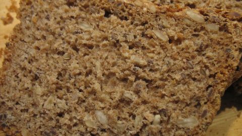 Dinkel-Vollkorn-Brot mit Haferflocken ist auf einem Holzbrett in Scheiben geschnitten, umgeben von natürlichem Licht.