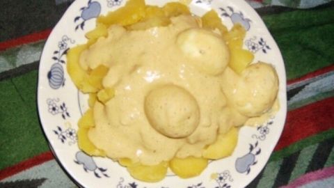 Ein Teller mit Salzkartoffeln und Eiern, umgeben von einer cremigen Senf-Meerrettichsoße, vor einem bunten Tischdecken.
